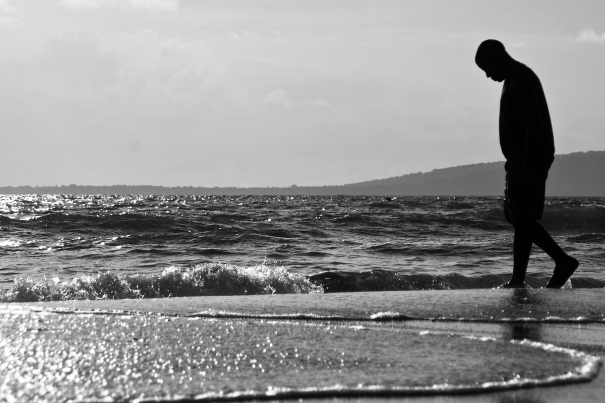 Silhouet van iemand die peinzend langs het water loopt
