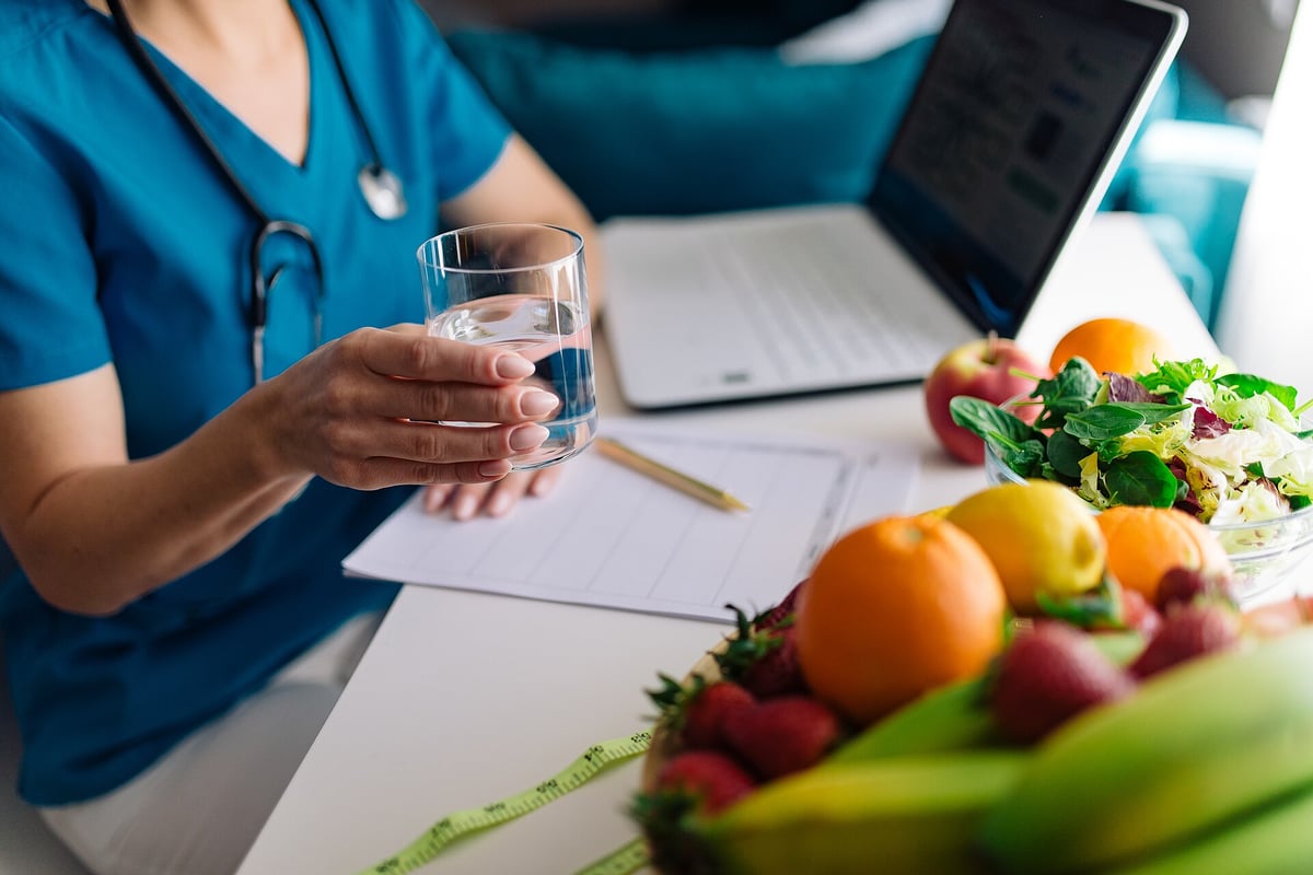 Iemand met een glas water naast vers fruit en groente